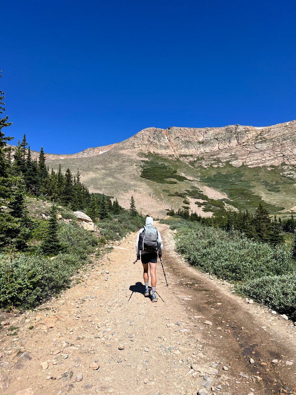 A hiker with trekking poles walks up a dirt road toward a rocky ridge